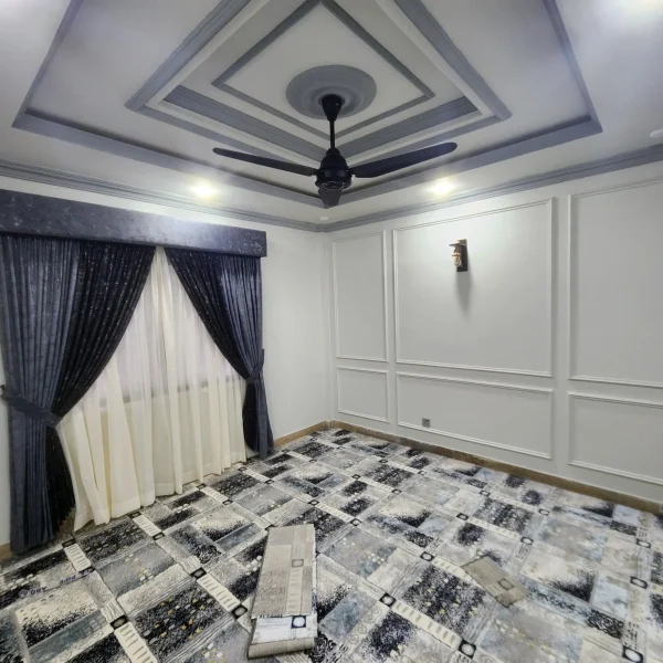 Modern lounge interior design with false ceiling, decorative wall panels, ceiling fan, elegant curtains, wall light, and stylish floor tiles.